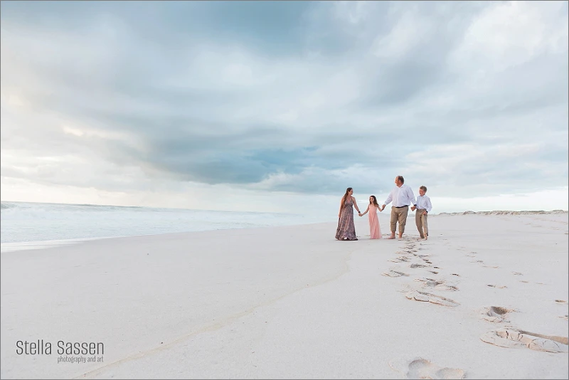 family walking on beach at sunset with dramatic skies in Cape Town during photo shoot