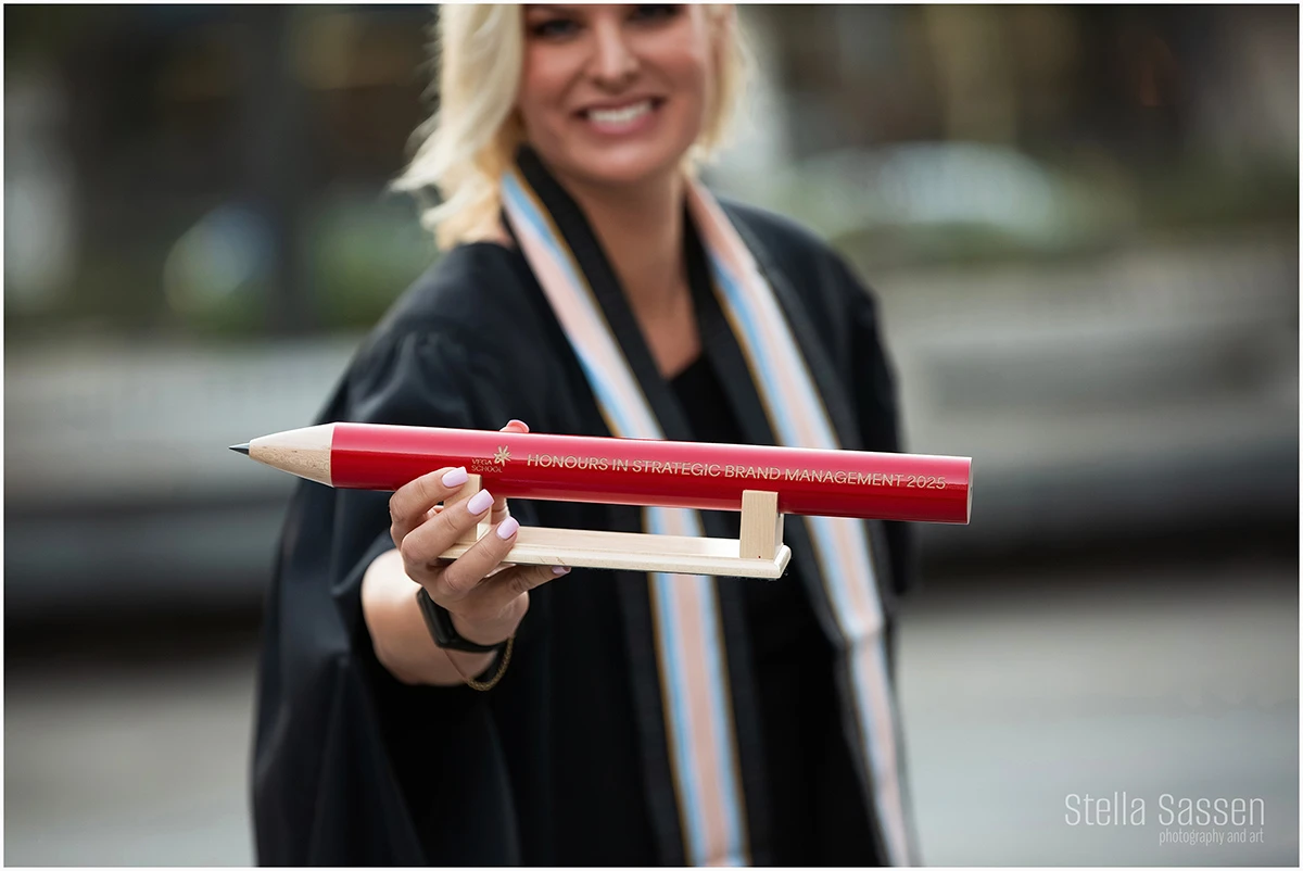 graduation image of a woman in a gown in an urban setting holding a prize